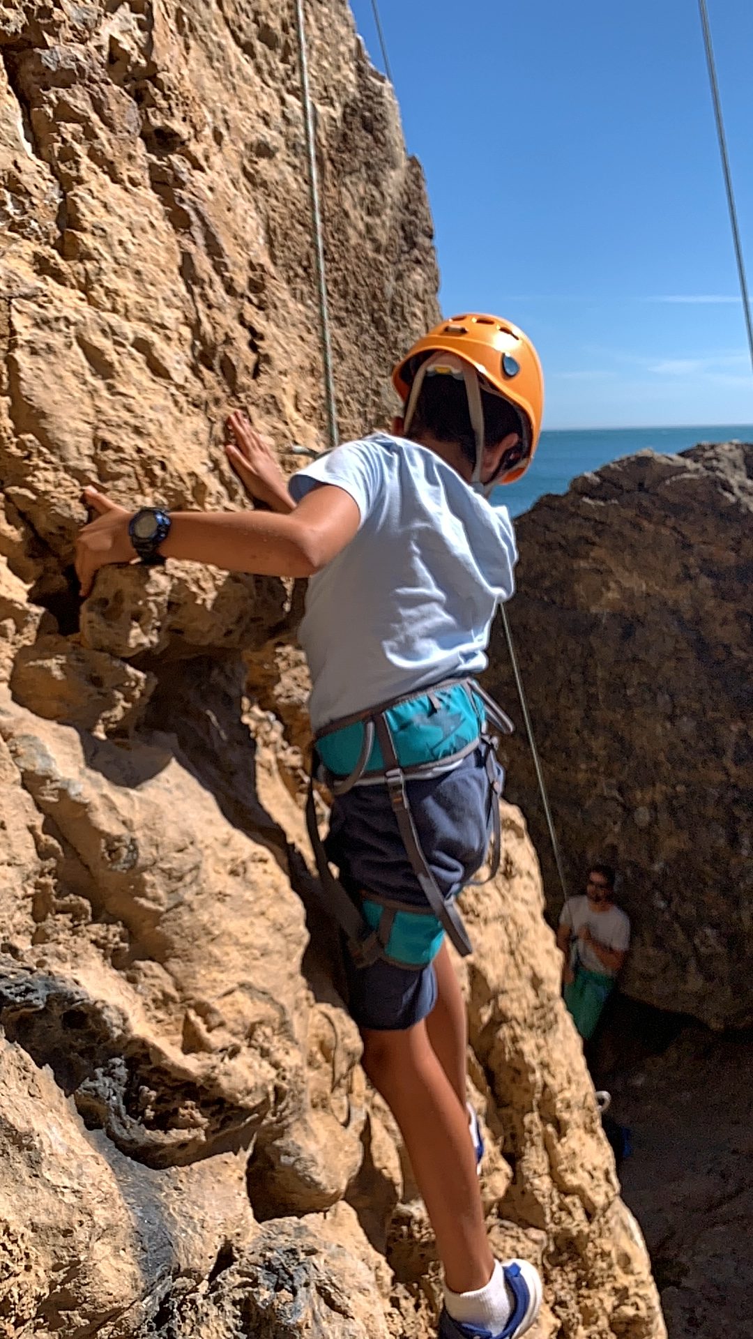 A helmeted climber working a route on coastal rock