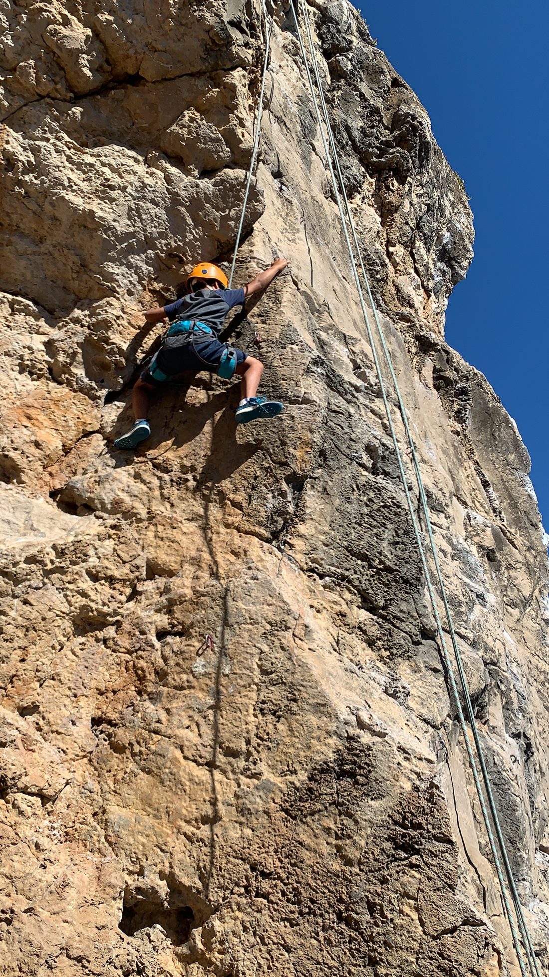 A helmeted student climbing a coastal crag while the group belays and watches from the base