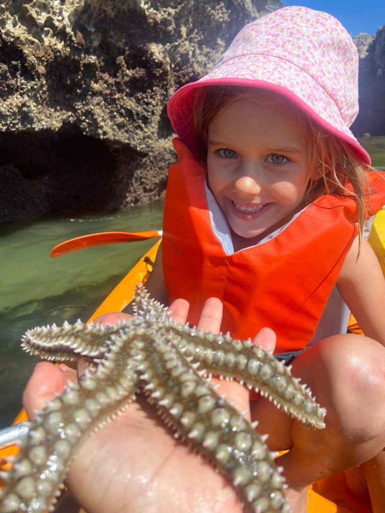 Girl in a kayak holding a starfish near a sea cave on the Cascais coast