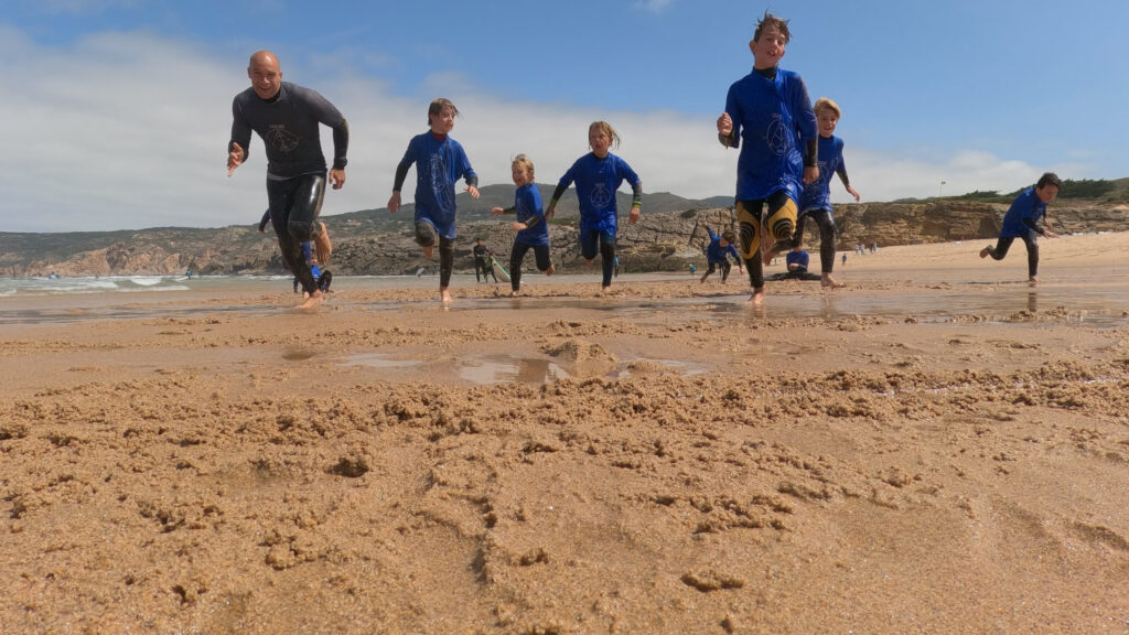 Kids camp group running on the beach in blue rash guards