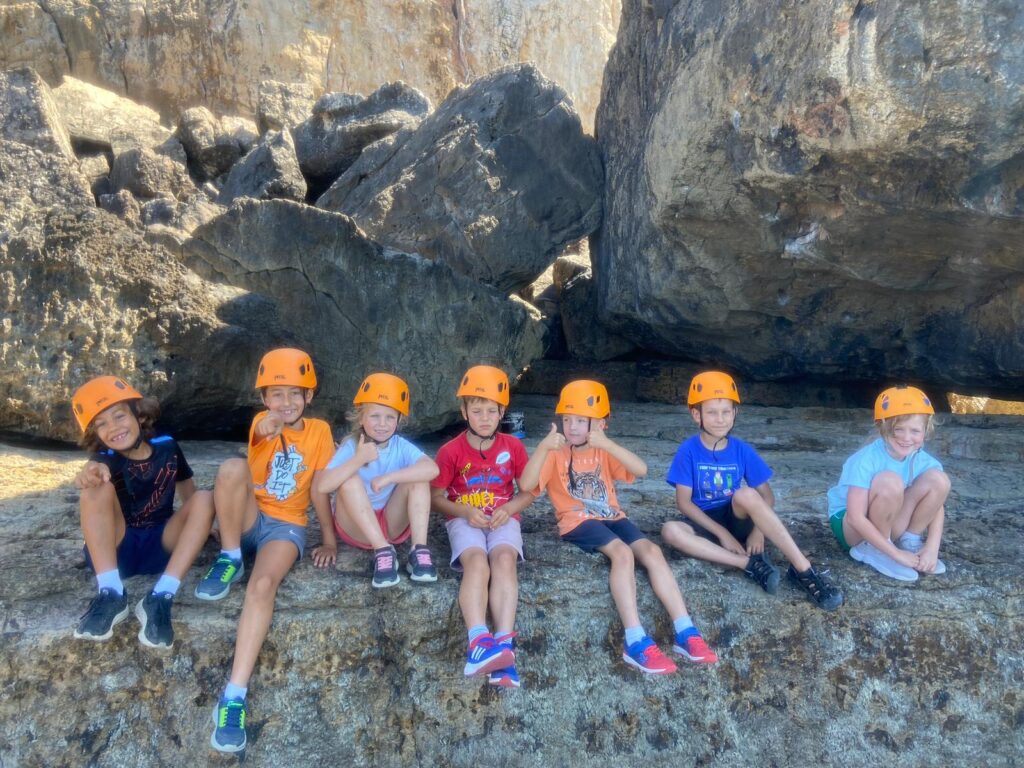 Kids camp group in orange climbing helmets sitting on rocks