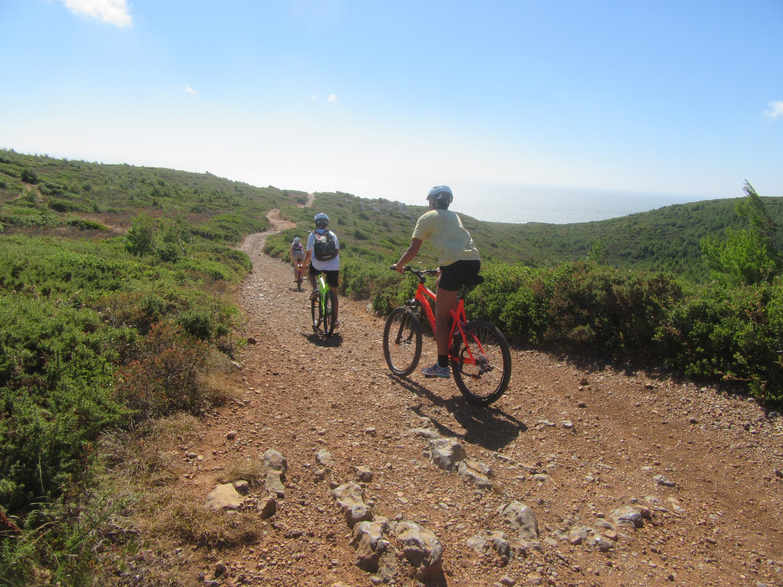 Mountain biker riding a gravel path below a cliffside estate