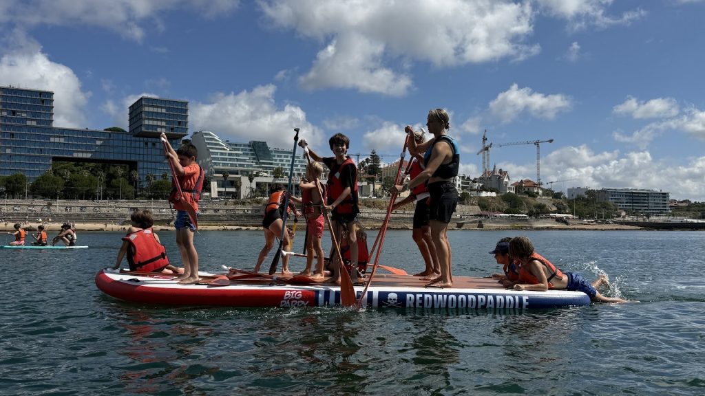 A group of kids and instructors standing on a giant SUP board